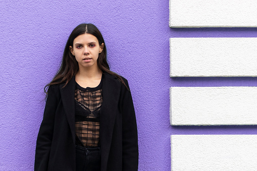 Portrait of a young stylish woman in black clothing. On a purple wall background.
