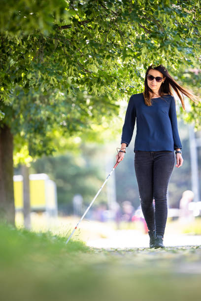 Blind woman walking on city streets, using her white cane stock photo