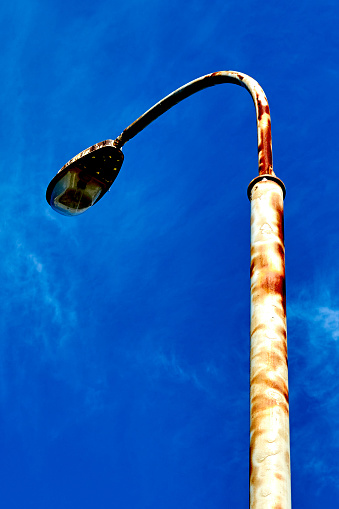 rusty modern street lamppost with a broken lamp against the blue sky.