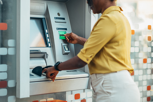 Beautiful young african american woman using an atm machine and a credit card while in the city