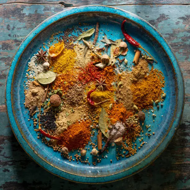Photo of Variety of colorful, organic, dried, vibrant Indian food spices on an old turquoise-colored ceramic plate.