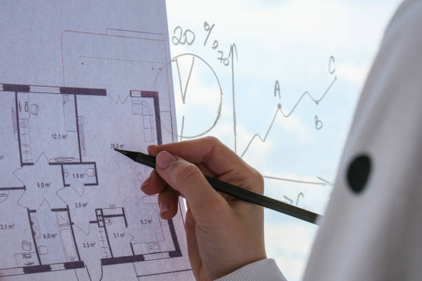 istock Female interior designer drawing house plan in office. Workplace Workspace window. Architect at work. Architectural construction plans with blueprints 1351006608