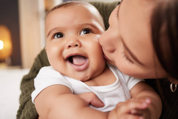 снимок молодой женщины, несущей своего ребенка дома - baby kissing mother lifestyles стоковые фото и изображения