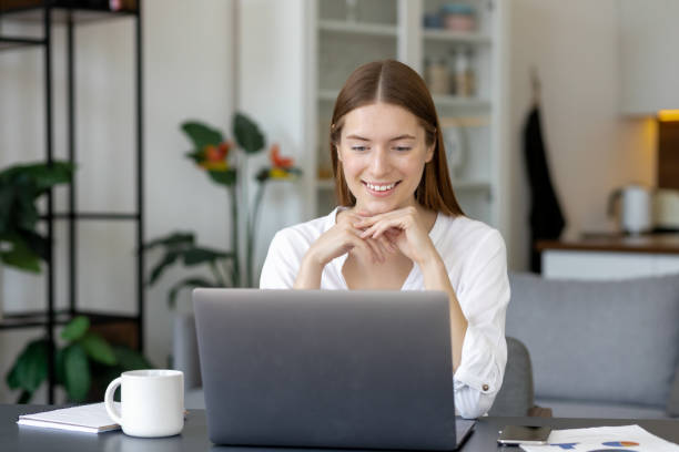 istock Smiling young woman working on laptop at home office. Remote studying or virtual training concept 1351008218