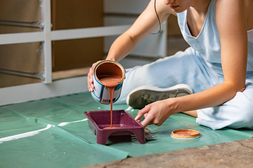 Close up of anonymous female sitting on the floor and pouring orange paint in a tray