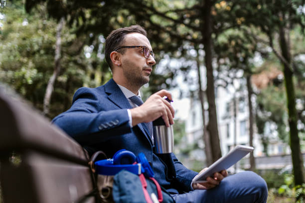 istock Young businessman sitting on park bench with tablet and having break 1351009198