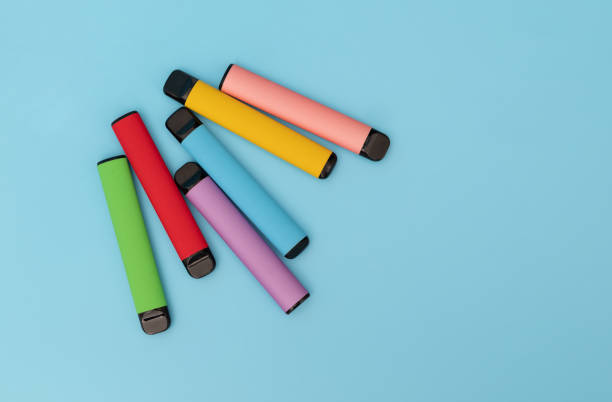 conjunto de coloridos cigarrillos electrónicos desechables sobre un fondo azul. el concepto de fumar moderno. vista superior - disposable fotografías e imágenes de stock