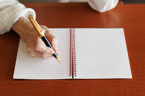 Elderly woman's hand with pen writing in a ruled notebook.