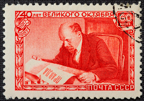 A postage stamp printed in the USSR depicts Vladimir Lenin Ulyanov reading the Pravda newspaper, 40th anniversary of the Great October Revolution, Lenin Series, circa 1957.