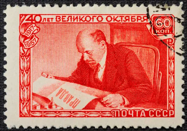 A postage stamp printed in the USSR depicts Vladimir Lenin Ulyanov reading the Pravda newspaper, 40th anniversary of the Great October Revolution, Lenin Series, circa 1957.