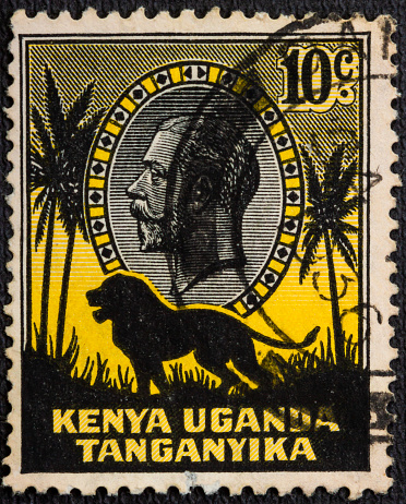 : a stamp printed in East Africa showing image of a lion and palm trees against the portrait of King George V, circa 1935.