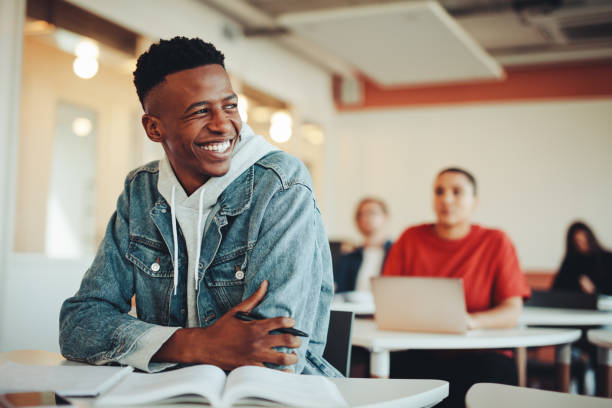 lächelnder männlicher student, der im klassenzimmer der universität sitzt - student stock-fotos und bilder