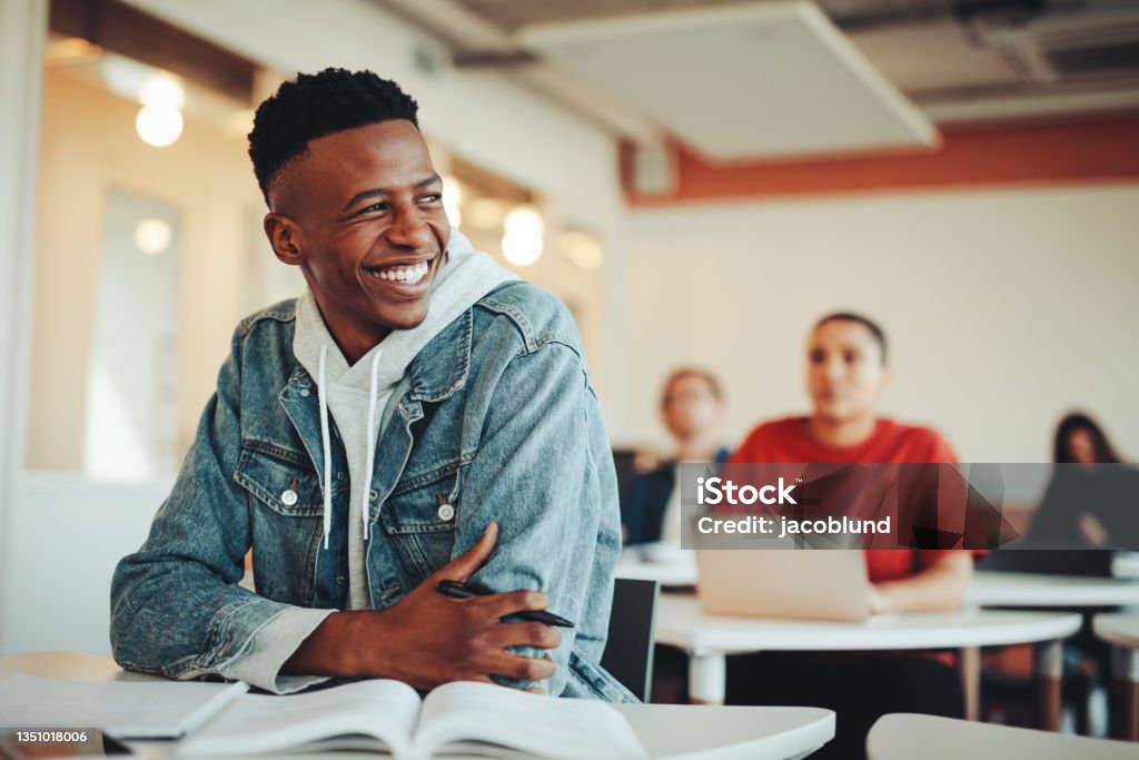 Smiling male student sitting in university classroom Male student sitting in university classroom looking away and smiling. Man sitting in lecture in high school classroom. University Student Stock Photo