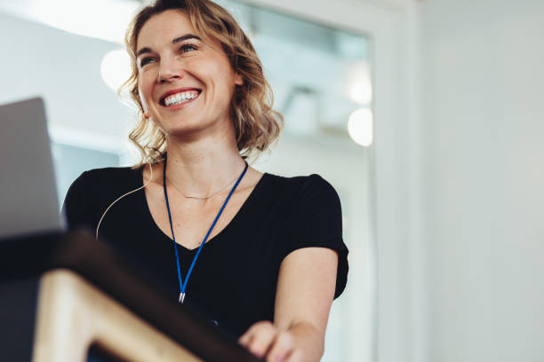 confident businesswoman standing at podium - podium lectern microphone white imagens e fotografias de stock