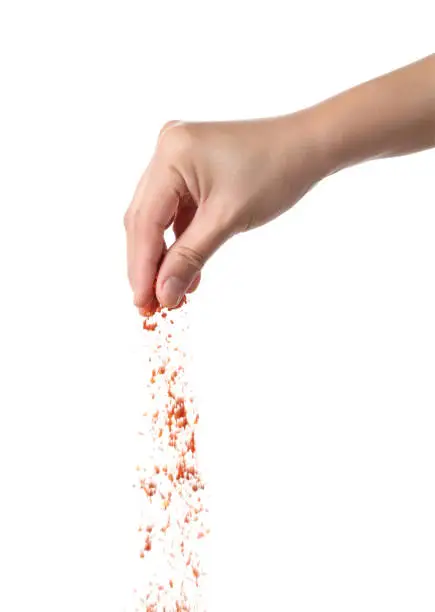 Photo of Hand sprinkling cayenne pepper isolated on white background