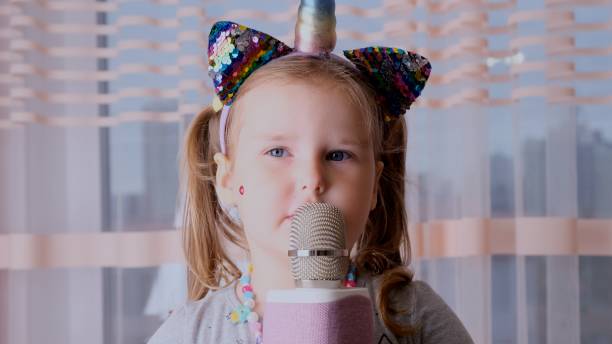 lustiges kleines mädchen 4-5 jahre alt, mit einem rand auf dem kopf und einem mikrofon in den händen, ein kind singt karaoke-musik, haben spaß bei einer veranstaltung zukünftige musiker laute stimme solo - cute 4 5 years little girls party stock-fotos und bilder