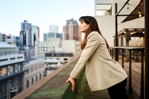 Shot of a mid adult businesswoman leaning to the office balcony wall and looking at the city space