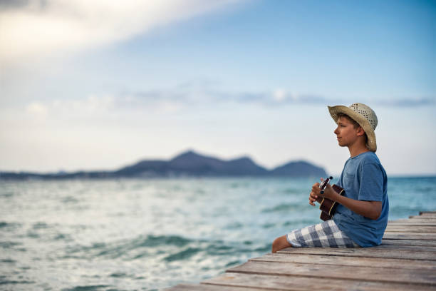 Teenage boy having fun sitting on pier and playing ukulele.\nCanon R5