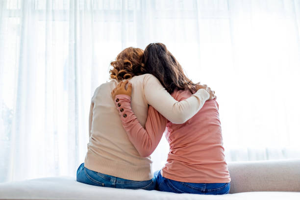 vista trasera de madre e hija abrazando sentadas en la cama - ánimo fotografías e imágenes de stock