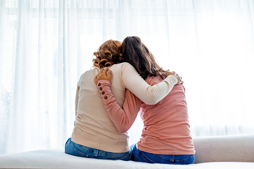 Rear view of mother and daughter embracing sitting on bed