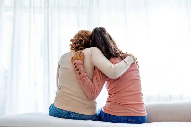 Photo of Rear view of mother and daughter embracing sitting on bed