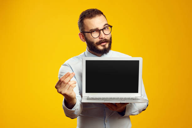 istock Bearded man holding laptop device while showing money gesture against yellow 1351029399