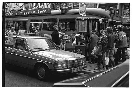 Street impression of Amsterdam in 1981. Trams and caps dominate the view. This is a scan of a negative. Crowd of people, locals and tourists on Leidsestraat in central Amsterdam.Business or shopping on this summer day,Tramway going to and arriving from the Amsterdam central train station.