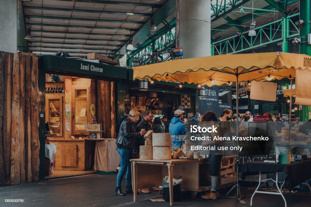 People at a cheese stand inside Borough Market, London, UK. London, UK - October 17, 2021: People at a cheese stand inside Borough Market, one of the largest and oldest food markets in London. Borough Market Stock Photo