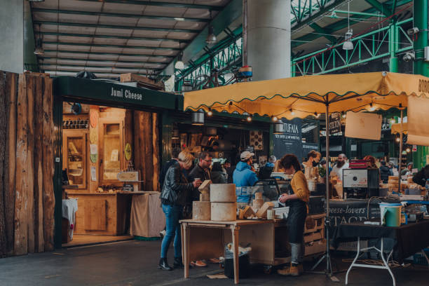 People at a cheese stand inside Borough Market, London, UK. London, UK - October 17, 2021: People at a cheese stand inside Borough Market, one of the largest and oldest food markets in London. small business saturday stock pictures, royalty-free photos & images
