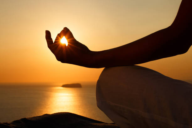 Meditating in Lotus position at sunset! Close up of unrecognizable person doing Yoga relaxation exercises in Lotus position on a hill above the sea at sunset. Copy space. meditating stock pictures, royalty-free photos & images