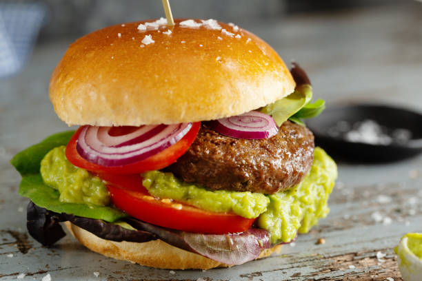 Burger with meat and avocado sauce served on wooden table