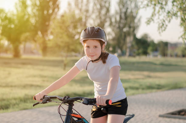 an 11-year-old girl in a protective sports helmet sits on a bicycle. girl with a bike in the park. children's sports and a healthy lifestyle - ten speed bicycle imagens e fotografias de stock