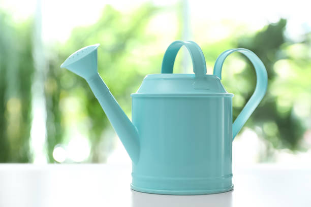 Light blue watering can on white table against blurred background