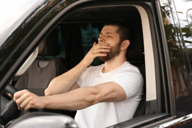 istock Tired man yawning while driving his modern car 1351041834