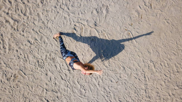 istock Drone view on woman in Extended side angle pose, casting shadow on sand 1351041881