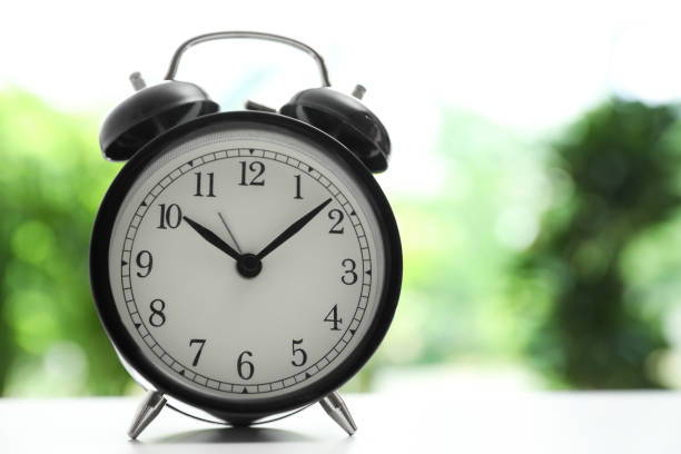 istock Modern black alarm clock on white table against blurred background. Space for text 1351041953