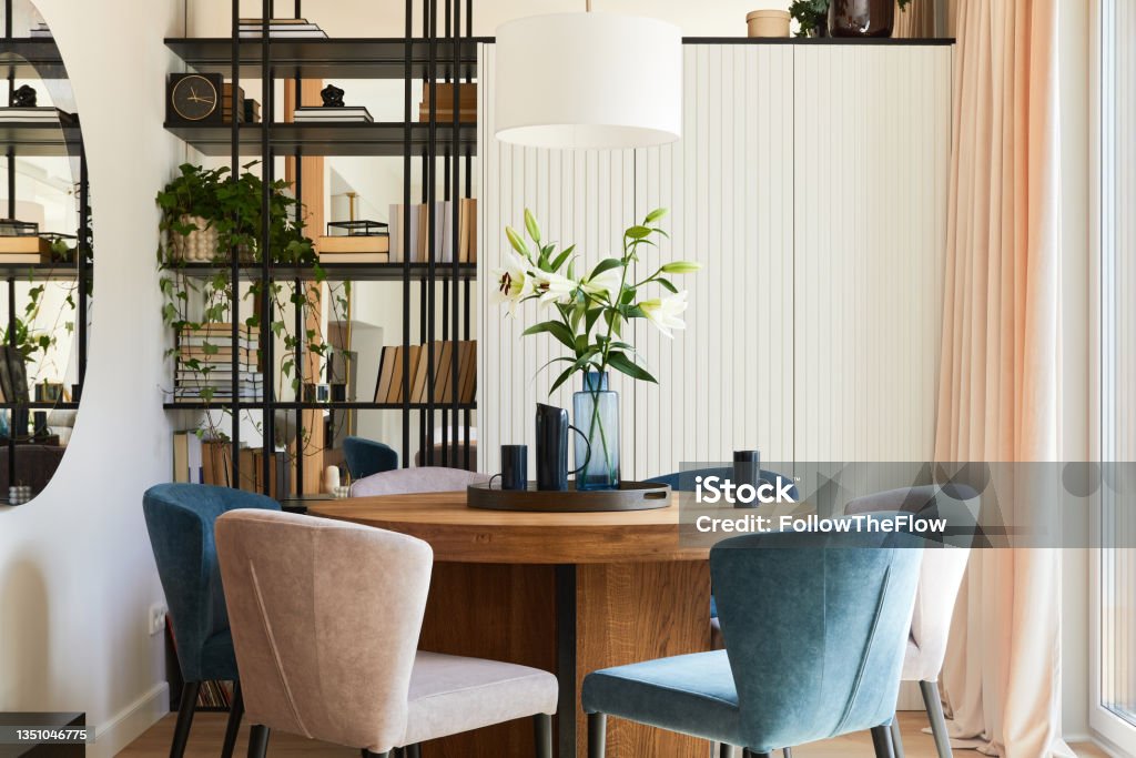 Elegant composition of stylish dining room interior design with velvet armchairs, design rounded wooden table and beautiful personal accessories. Glamour interior design inspiration. Template. Apartment Stock Photo