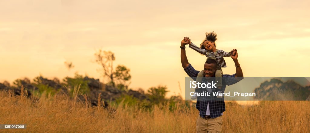 Happy African family child daughter riding the neck father and running on meadow nature on silhouette lights sunset.  Travel and Family Concept, Happy African family child daughter riding the neck father and running on meadow nature on silhouette lights sunset.  Travel and Family Concept, copy space for banner Family Stock Photo