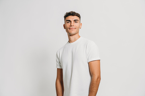 Portrait of a young adult man against a white background. He's standing, looking at camera.