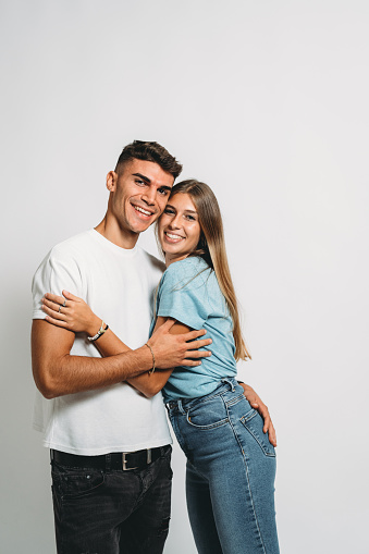 Portrait of a young adult couple against a white background. They are embracing together.