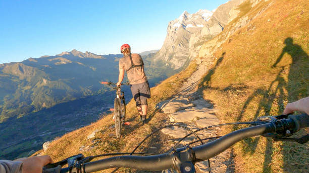 istock Man pushes mountain biker along trail in the Alps 1351048840