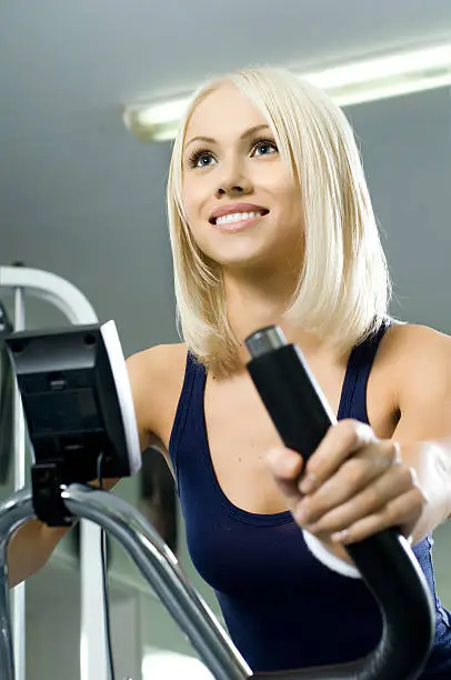 happy cutie athletic girl ,  execute exercise on exercise bicycle  and smile, in  sport-hall, close face