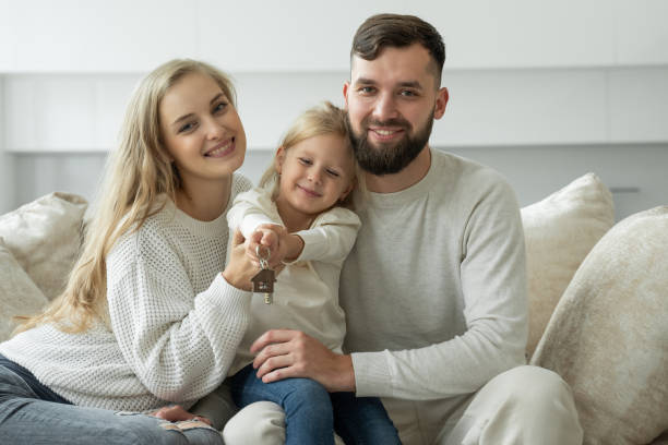 Little girl holds the keys to a new family home in her hands. Portrait of a smiling young married couple and a cute girl showing the keys stock photo