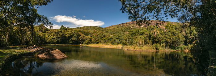 Panorama of natural landscape with lake in the mountain of Pedra Grande. Water mirror, local vegetation, mountain and blue sky with clouds. Atibaia, Brazil.
