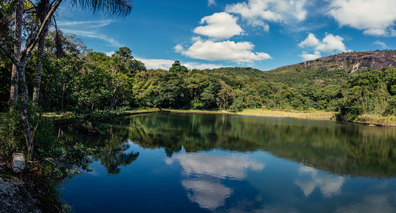 Panorama of natural landscape with lake in the mountain of Pedra Grande. Water mirror, local vegetation, mountain and blue sky with clouds. Atibaia, Brazil.