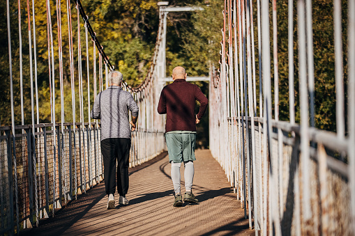 Two men, senior men jogging together on a small bridge on autumn day outdoors.