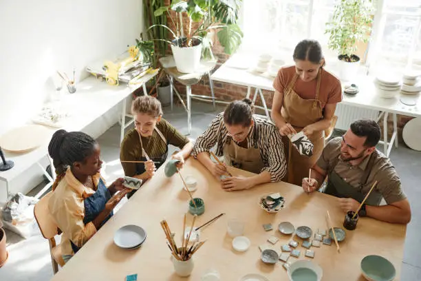 High angle shot of creative group of people decorating ceramics in pottery workshop, copy space