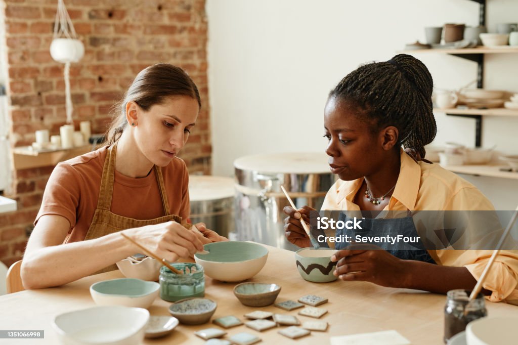 Young Women in Pottery Studio Warm toned portrait of two young women enjoying pottery workshop in cozy studio, copy space Art Therapy Stock Photo
