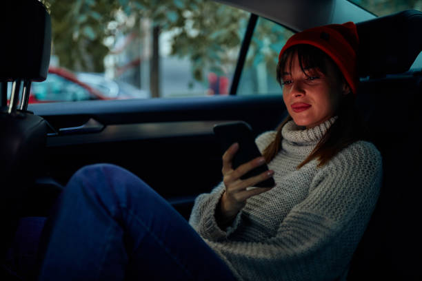 istock Young woman sitting on backseat in car and using phone 1351068577