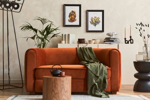 Creative composition of stylish living room interior with mock up poster frame, orange sofa, beige commode, coffee table and stylish personal accessories. Artistic space. Template. stock photo